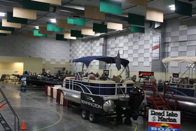 Boat show inside The Pavilion Expo Hall featuring pontoon boats on display with vendor signage and lighting overhead.