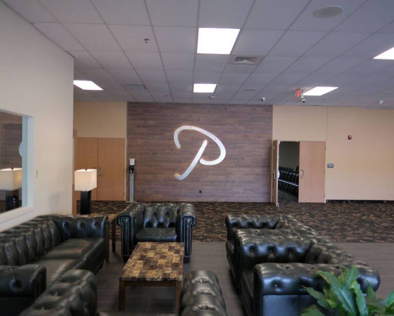 Front lobby of The Pavilion featuring black leather couches, wood accent wall with large silver ‘P’ logo, and modern lighting. Contact The Pavilion Today for Rentals