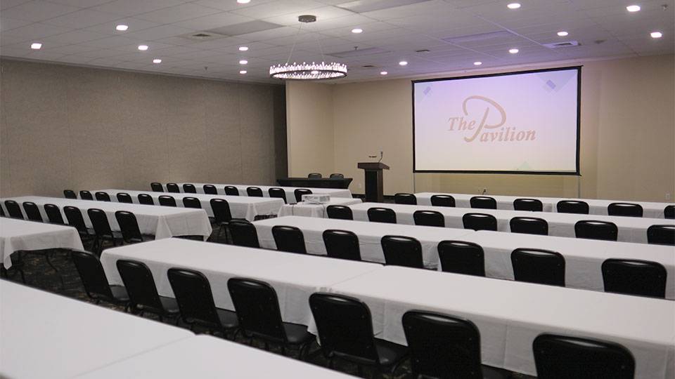 Meeting room at The Pavilion arranged classroom-style with tables, chairs, podium, and presentation screen.
