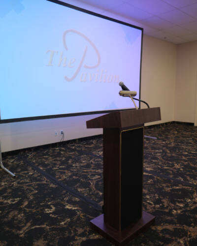 Podium and microphone in a meeting room at The Pavilion with presentation screen in the background.